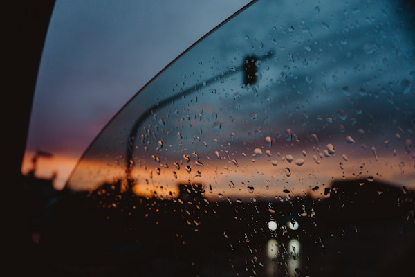Raindrops on a car window at dusk, the sky fading from blue to orange