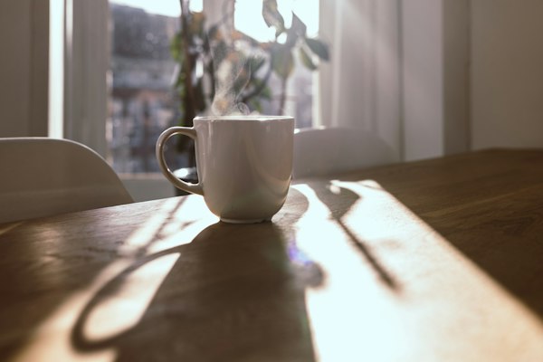 A steaming mug on a wooden table in morning sunlight